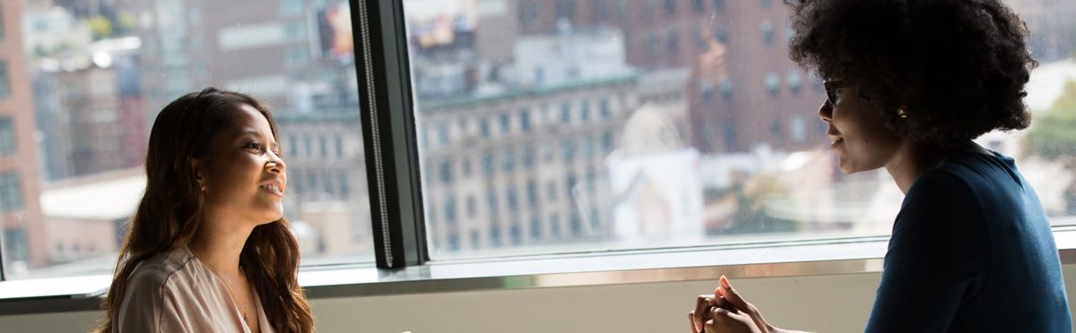 Two women in a friendly conversation by a window